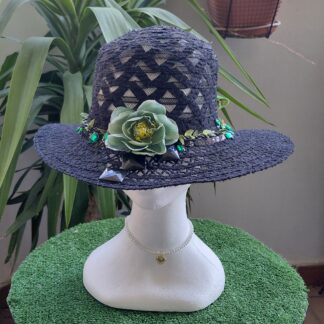 Sombrero negro de encaje de algodón con tira negra tipo cuero con hojas verdes de tela, tiras de lentejuelas, plumas negras, pedrería negra y verde botella tipo cristal